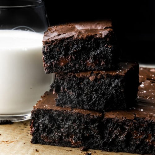 black cocoa brownies with a cup of milk next to them.