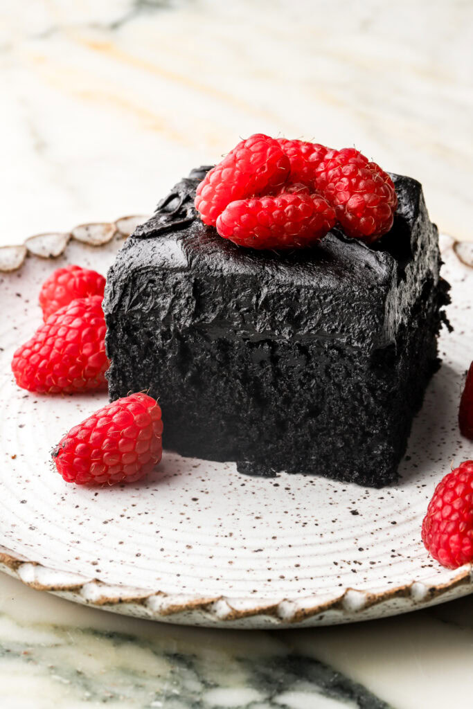 slice of black cocoa sheet cake on a plate topped with fruit
