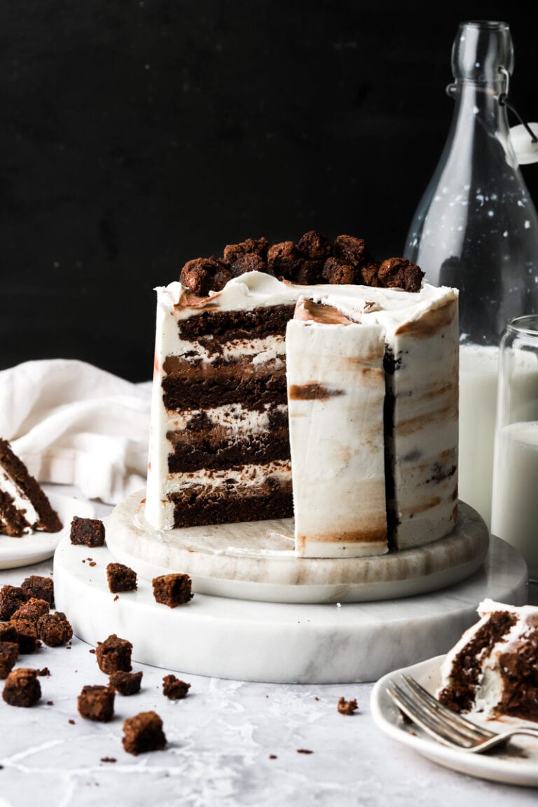 brownie cake frosted with cream cheese frosting, a slice removed and little brownies and milk on the side