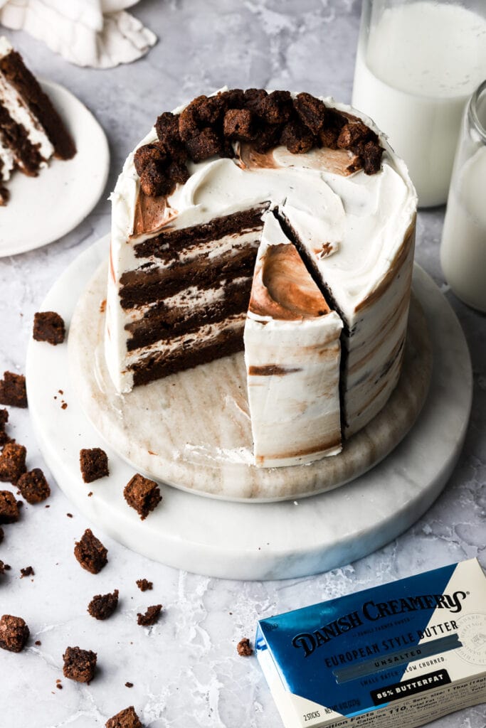 brownie cake on a marble board frosted with cream cheese frosting and topped with mini brownies