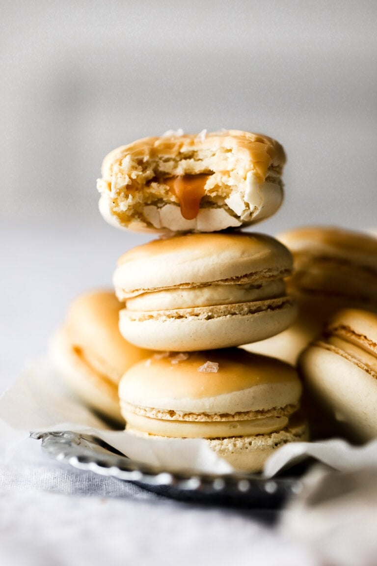 salted caramel macarons stacked with a bite taken out and a drip of caramel falling
