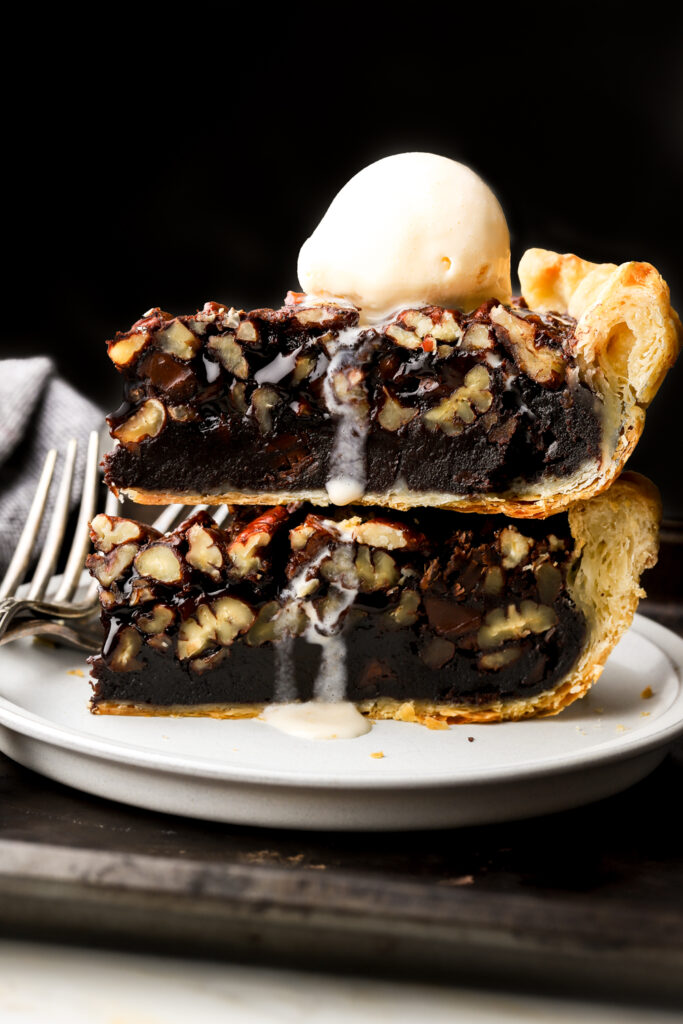 two slices of chocolate pecan pie stacked on a plate with a scoop of vanilla ice cream