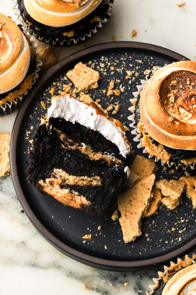 a bite taken out of a chocolate s'mores cupcake on a plate