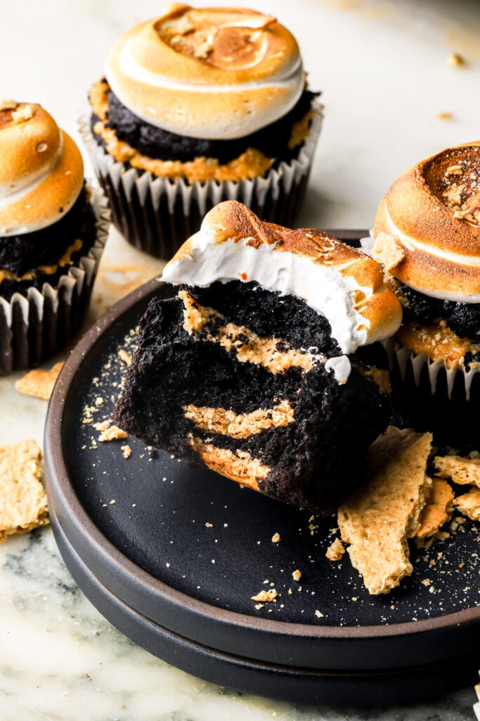 a bite taken out of a chocolate s'mores cupcake on a plate