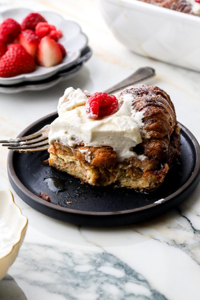 slice of french toast on a plate topped with whipped cream and strawberries next to it