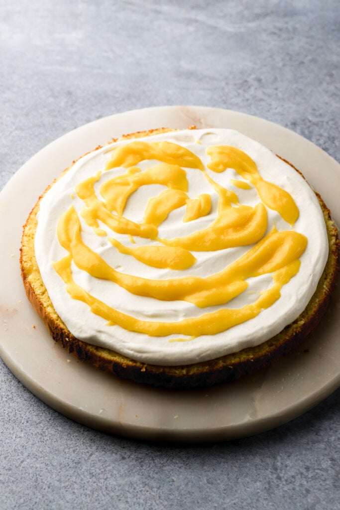 lemon curd swirled on top of whipped cream on top of cake layer