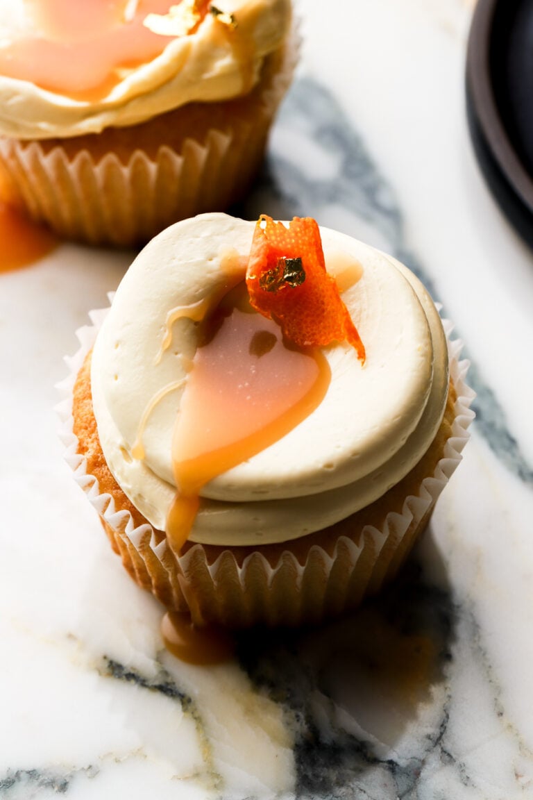 orange cupcakes topped with orange buttercream, orange caramel sauce and a slice of orange peel