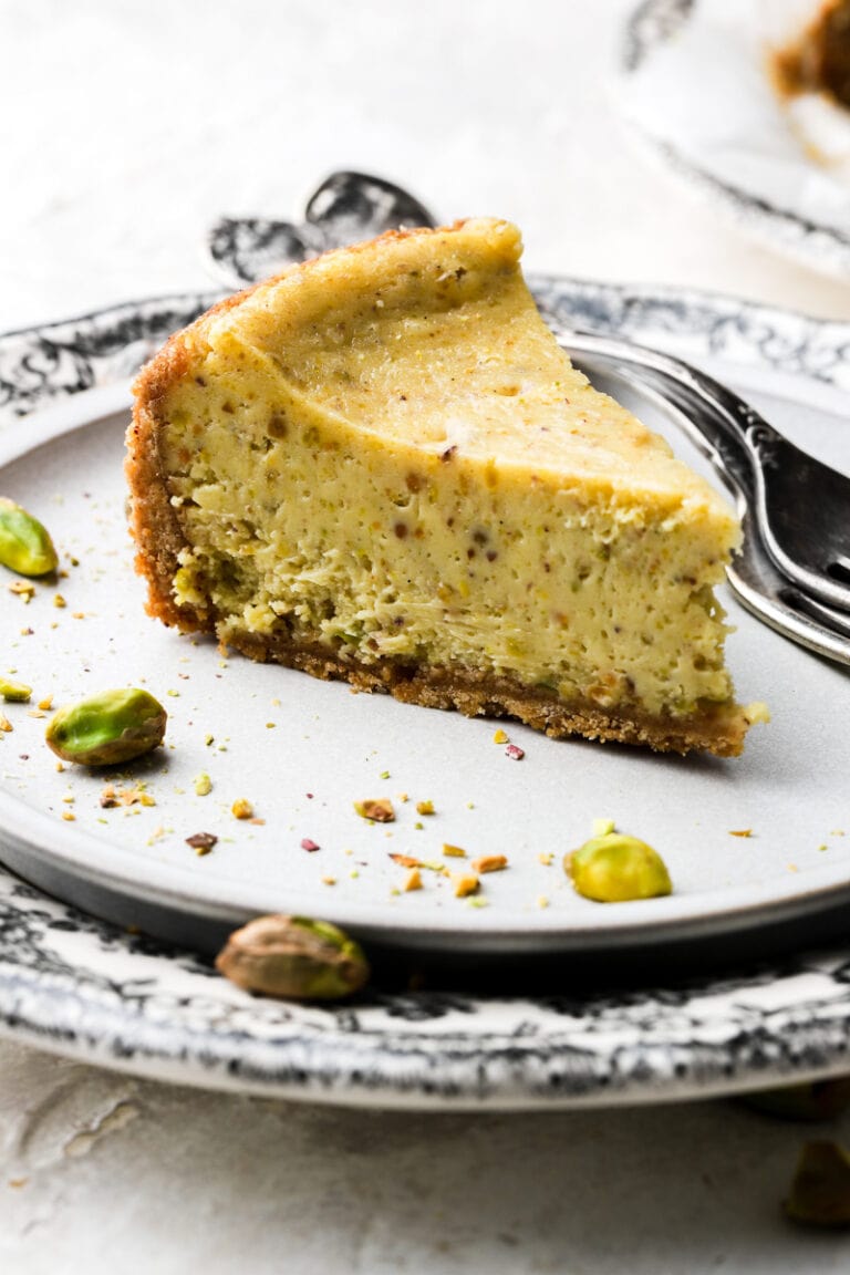 slice of pistachio cheesecake on a plate with pistachios on the side