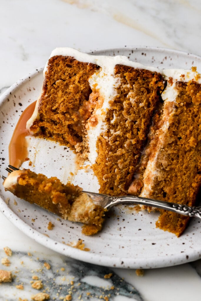slice of pumpkin cake with cream cheese frosting and caramel sauce on a plate with a bite taken out