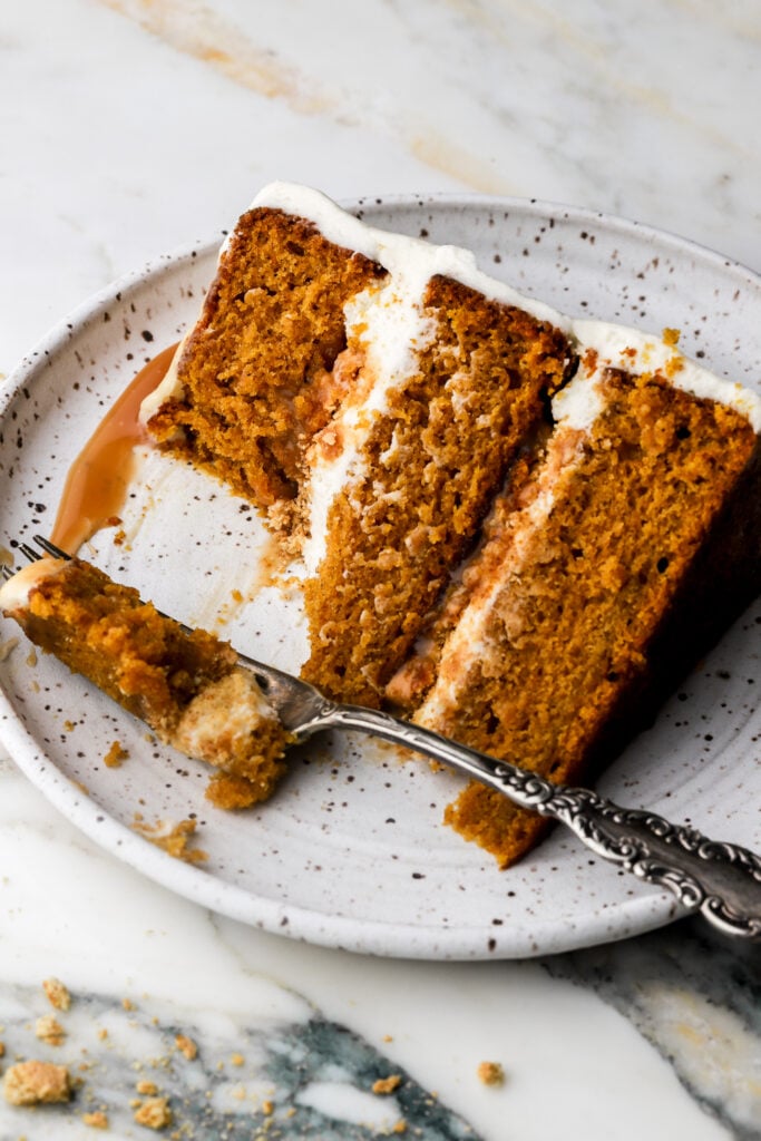 slice of pumpkin cake with cream cheese frosting and caramel sauce on a plate with a bite taken out