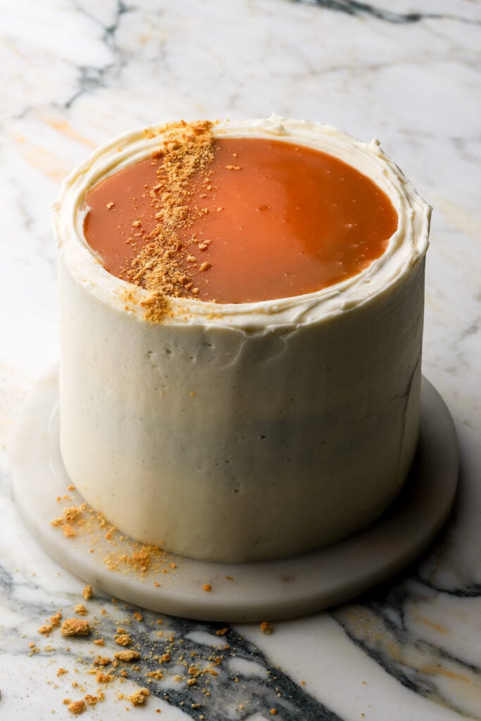 pumpkin cake fully frosted with cream cheese frosting and topped with salted caramel sauce and crushed graham crackers