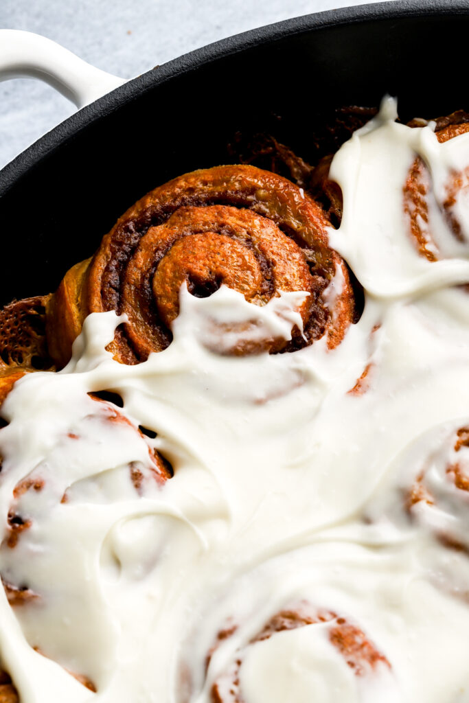 pumpkin cinnamon rolls still in the pan with cream cheese frosting covering most but not all the rolls