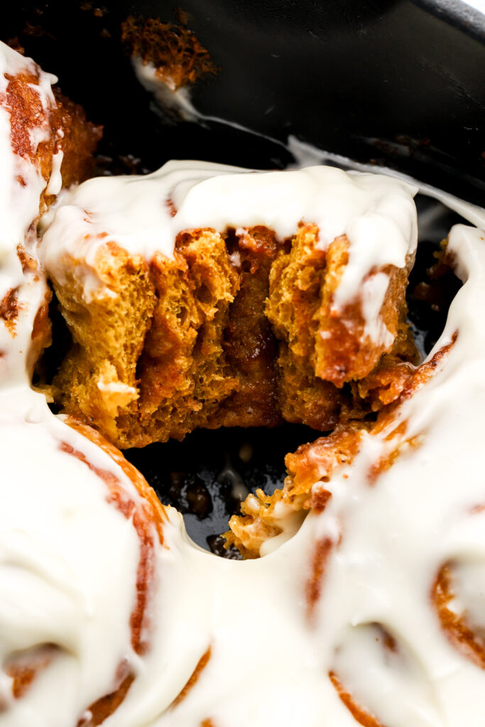 close up of a pumpkin cinnamon roll half eaten still in the pan surrounded by other rolls