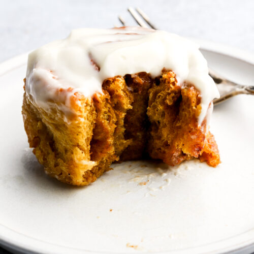 pumpkin cinnamon rolls with cream cheese frosting on a plate with a bite taken out