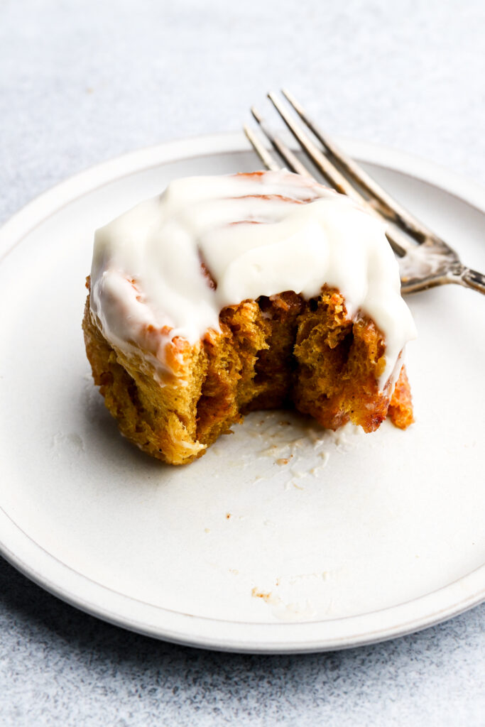 pumpkin cinnamon roll on a plate half eaten with a fork