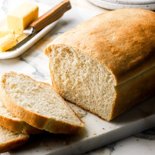 sandwich bread with two slices cut and butter in the background