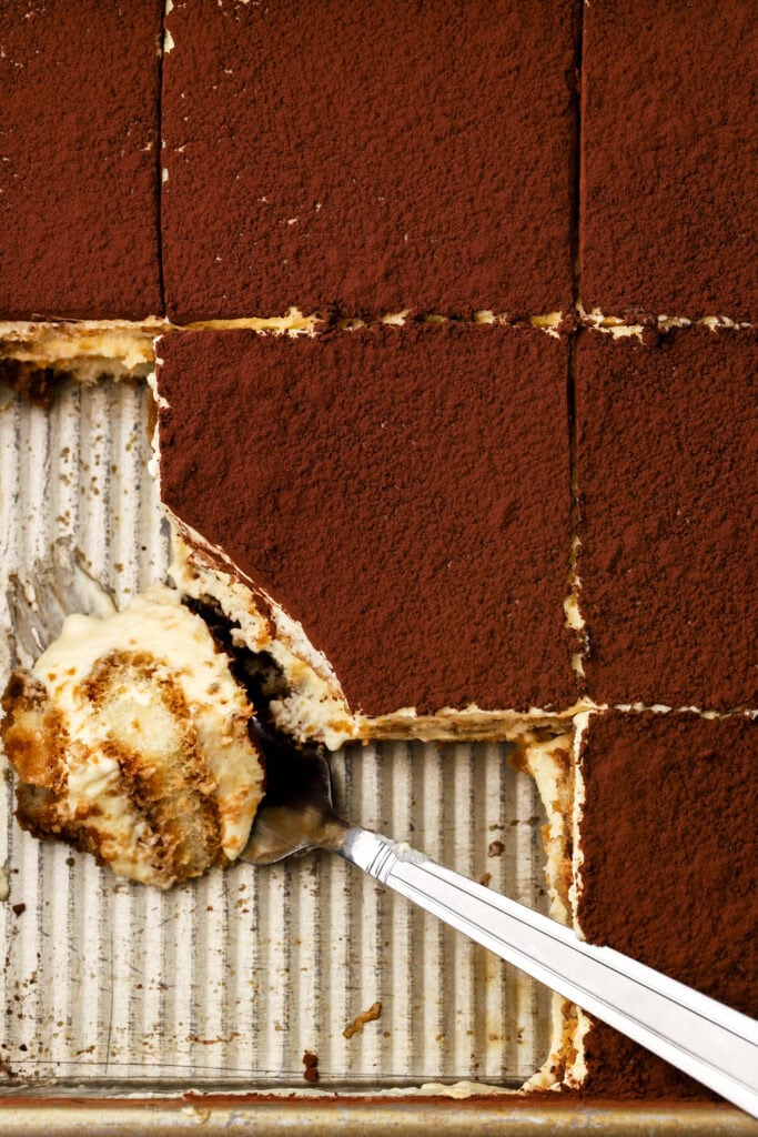 a bite taken out of a slice of tiramisu in a tray