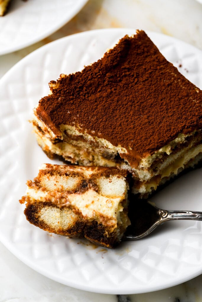 slice of tiramisu on a plate with a bite on a fork