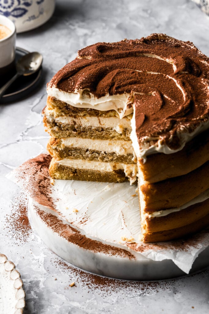 tiramisu cake with slices taken out, teapot in the back