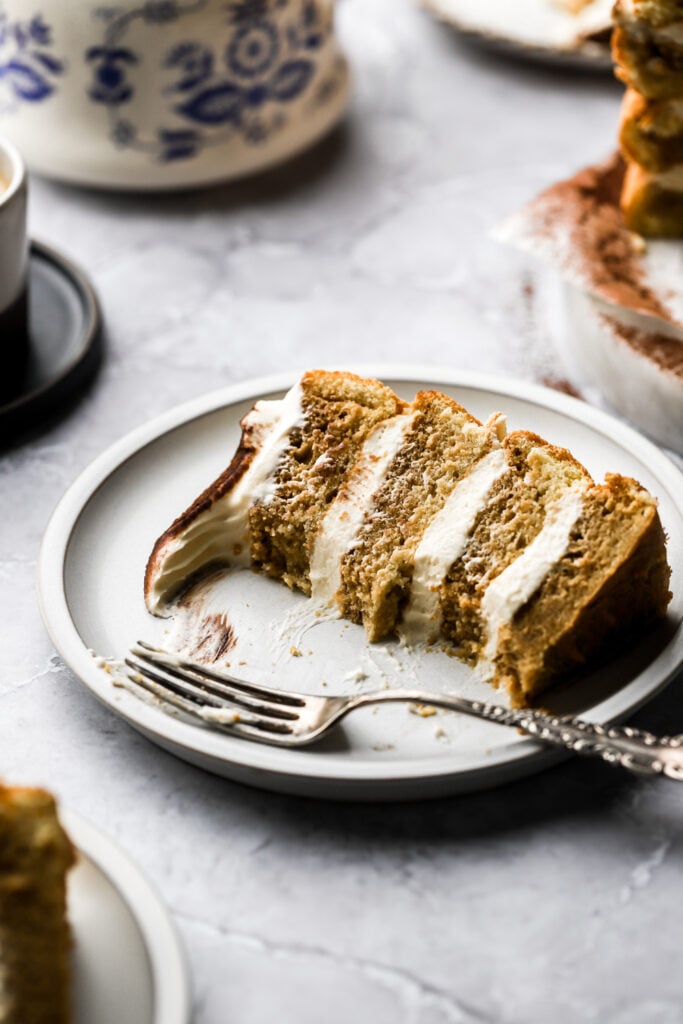 slice of cake on a plate with tea pot behind it