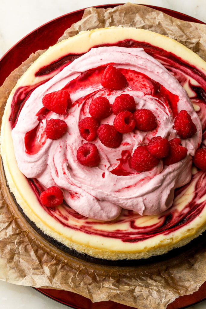 white chocolate raspberry cheesecake topped with raspberry whipped cream and fresh raspberries