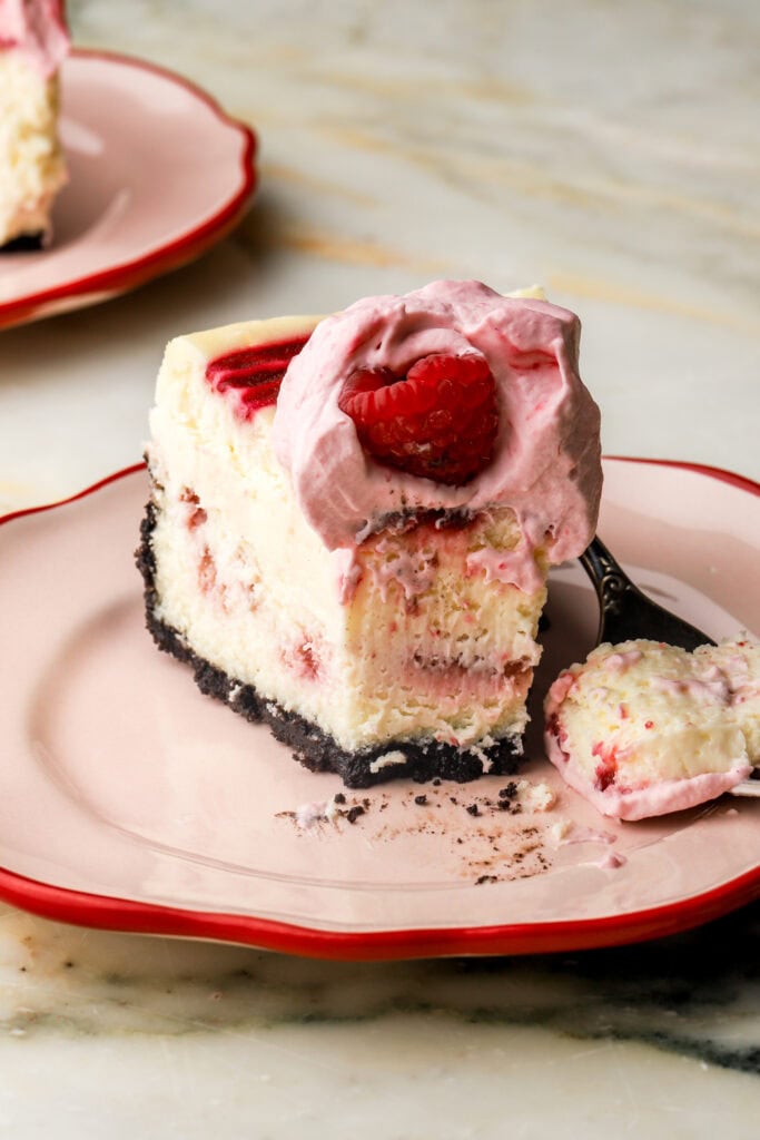 close up of a slice of white chocolate raspberry cheesecake with a bite taken out 
