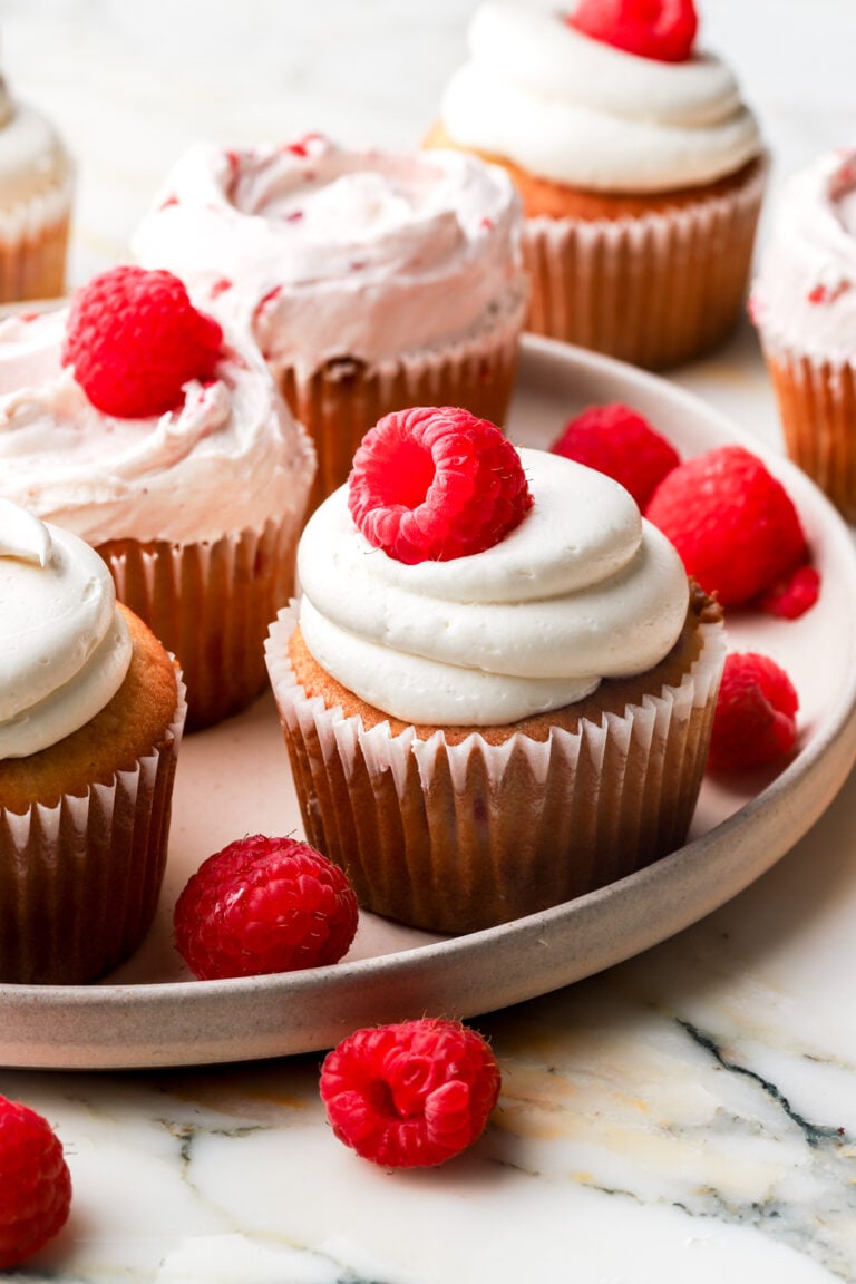 white chocolate raspberry cupcakes on a plate with raspberries